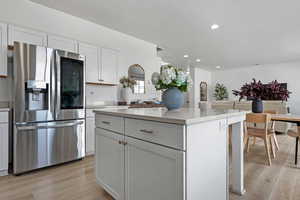 Kitchen with stainless steel fridge, light wood-type flooring, a kitchen island, and white cabinets