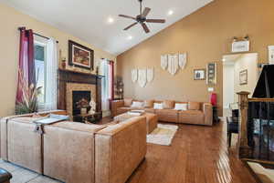 Living room with ceiling fan, a stone fireplace, high vaulted ceiling, and light hardwood / wood-style floors