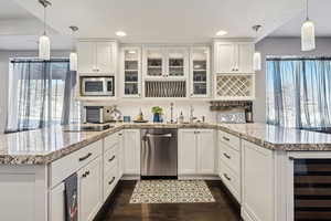 Kitchen with pendant lighting, appliances with stainless steel finishes, beverage cooler, and white cabinets