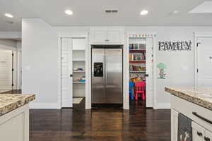 Kitchen featuring white cabinetry, light stone countertops, dark hardwood / wood-style floors, and stainless steel fridge