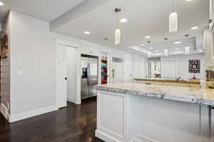 Kitchen with decorative light fixtures, stainless steel fridge with ice dispenser, a raised ceiling, light stone countertops, and white cabinets