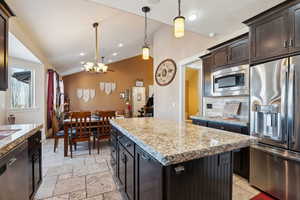 Kitchen with stainless steel appliances, a center island, decorative backsplash, decorative light fixtures, and vaulted ceiling