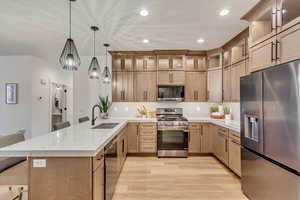 Kitchen with appliances with stainless steel finishes, decorative light fixtures, sink, light wood-type flooring, and a breakfast bar