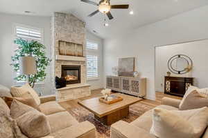 Living room featuring light wood-type flooring, ceiling fan, vaulted ceiling, and a stone fireplace