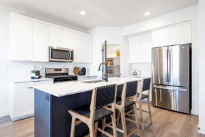 Kitchen with light hardwood / wood-style floors, sink, white cabinetry, a kitchen island with sink, and appliances with stainless steel finishes