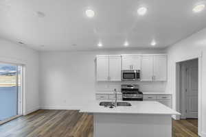 Kitchen featuring hardwood / wood-style floors, sink, white cabinetry, a kitchen island with sink, and appliances with stainless steel finishes