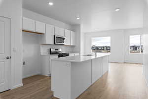 Kitchen with sink, appliances with stainless steel finishes, an island with sink, and white cabinetry