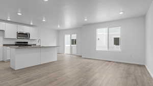 Kitchen featuring white cabinets, a healthy amount of sunlight, stove, and an island with sink