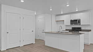 Kitchen with sink, light hardwood / wood-style flooring, a kitchen island with sink, white cabinets, and range