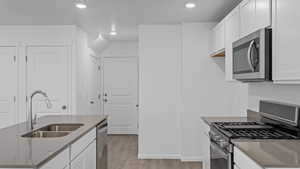 Kitchen featuring appliances with stainless steel finishes, light hardwood / wood-style flooring, white cabinetry, and sink