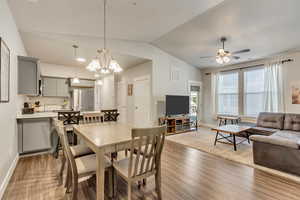 Dining room featuring ceiling fan with notable chandelier, dark wood-type flooring, and vaulted ceiling