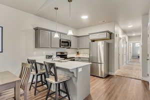 Kitchen with light hardwood / wood-style flooring, decorative light fixtures, stainless steel appliances, kitchen peninsula, and gray cabinetry