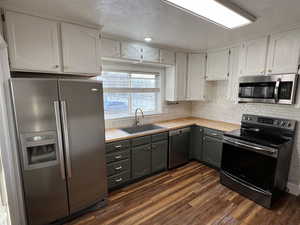 Kitchen with dark hardwood / wood-style flooring, sink, stainless steel appliances, and white cabinetry