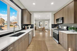 Kitchen with decorative backsplash, sink, appliances with stainless steel finishes, and light hardwood / wood-style flooring