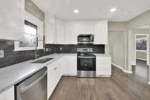 Kitchen with hardwood / wood-style floors, appliances with stainless steel finishes, white cabinetry, sink, and plenty of natural light