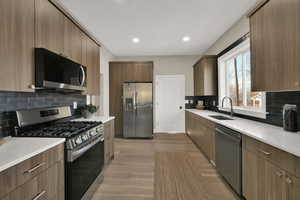 Kitchen with tasteful backsplash, light wood-type flooring, appliances with stainless steel finishes, and sink