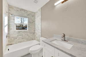 Full bathroom with toilet, tiled shower / bath combo, and vanity