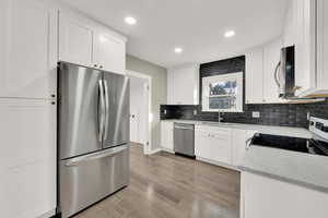 Kitchen featuring tasteful backsplash, light hardwood / wood-style floors, sink, stainless steel appliances, and white cabinets