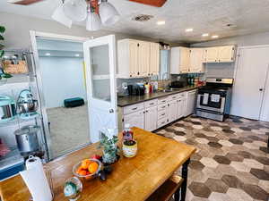 Kitchen with a textured ceiling, dishwasher, white cabinetry, stainless steel gas range, and sink