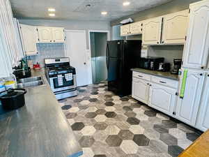 Kitchen with sink, backsplash, white cabinetry, a textured ceiling, and black appliances