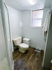 Bathroom featuring hardwood / wood-style flooring, a textured ceiling, toilet, and an enclosed shower