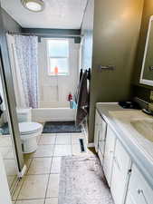 Full bathroom featuring a textured ceiling, tile patterned flooring, vanity, shower / tub combo, and toilet