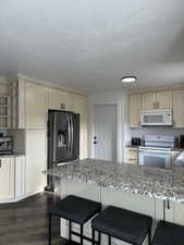 Kitchen featuring dark hardwood / wood-style floors, white appliances, a kitchen breakfast bar, cream cabinetry, and light stone counters