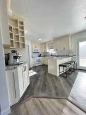 Kitchen with light stone countertops, white appliances, a kitchen breakfast bar, dark hardwood / wood-style floors, and cream cabinetry