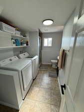 Laundry room with light tile patterned flooring, a textured ceiling, and washing machine and clothes dryer