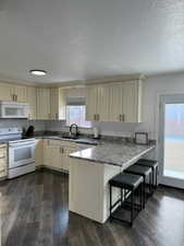 Kitchen featuring kitchen peninsula, sink, white appliances, dark wood-type flooring, and a breakfast bar area