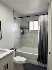 Full bathroom featuring a textured ceiling, vanity, toilet, shower / tub combo with curtain, and hardwood / wood-style flooring