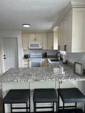 Kitchen featuring a breakfast bar, kitchen peninsula, sink, and white appliances