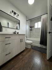 Full bathroom featuring toilet, shower / bathtub combination with curtain, wood-type flooring, and vanity