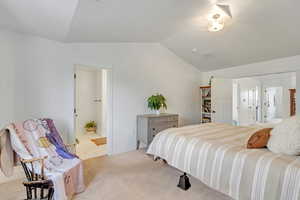 Carpeted bedroom with connected bathroom and vaulted ceiling