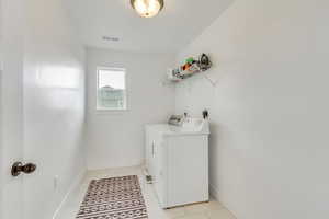 Clothes washing area with washing machine and dryer and light tile patterned floors