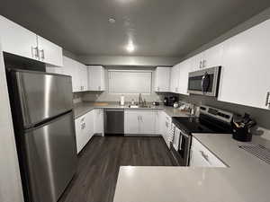 Kitchen with sink, white cabinetry, dark wood-type flooring, a textured ceiling, and stainless steel appliances