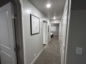 Hallway with a textured ceiling and dark colored carpet