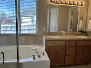 Master bathroom featuring a jetted bathtub, double vanity, and a healthy amount of sunlight