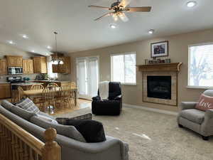 Living room/great room area featuring a tiled fireplace, light colored carpet, vaulted ceiling, and ceiling fan