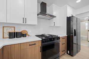 Kitchen featuring stainless steel refrigerator with ice dispenser, gas stove, backsplash, wall chimney range hood, and white cabinets