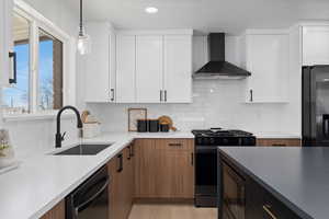 Kitchen with pendant lighting, black appliances, white cabinetry, wall chimney range hood, and sink