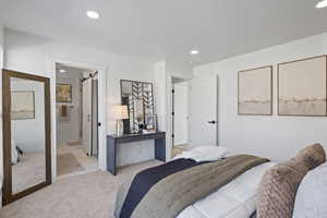 Carpeted bedroom featuring a textured ceiling, ensuite bathroom, and a barn door