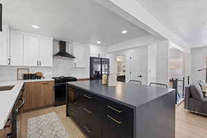 Kitchen featuring wall chimney range hood, a center island, black appliances, decorative backsplash, and white cabinets