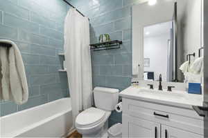 Full bathroom featuring tile walls, toilet, vanity, and shower / bath combination with curtain