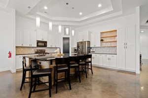 Kitchen with a kitchen bar, appliances with stainless steel finishes, a center island with sink, and a raised ceiling