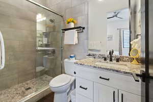 Bathroom featuring toilet, vanity, ceiling fan, and a shower with door