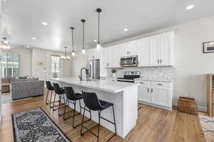 Kitchen featuring large kitchen island, white cabinetry, stainless steel appliances, backsplash.