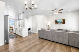 Living room featuring ceiling fan with notable chandelier, sink, and light hardwood / wood-style flooring