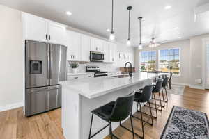 Kitchen with an island with sink, stainless steel appliances, a kitchen breakfast bar, white cabinets, and sink