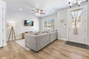 Living room featuring ceiling fan with notable chandelier and light wood-type flooring